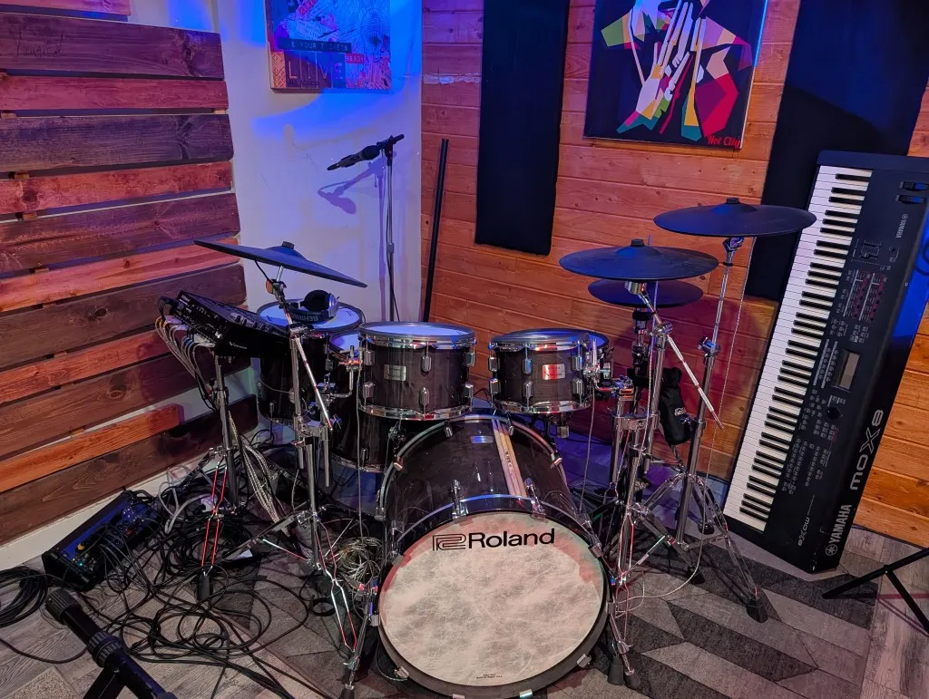 Studio A Roland electronic drum kit and Yamaha keyboard under blue light